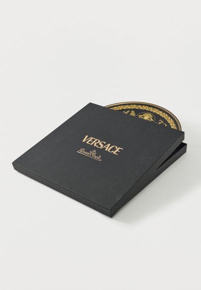 Μια μαύρη κουτί Versace Rosenthal μερικώς ανοιχτή αποκαλύπτοντας ένα στρογγυλό πιάτο με περίπλοκο χρυσό και μαύρο σχέδιο Μεδουσας στο εσωτερικό.