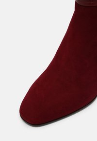 Gros plan sur une botte en suède rouge foncé avec un bout pointu et une semelle noire lisse.