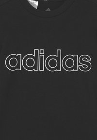 Musta Adidas-t-paita, jossa brändin nimi on suurilla valkoisilla ääriviivoilla kirjoitettuna rinnan keskelle.
