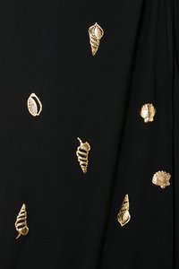 Svart stoff med gullbroderte skjelldesign som er spredd over overflaten, med forskjellige former og teksturer.