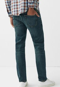 Jeans din denim de culoare bleu închis, cu un fason drept, având două buzunare pe spate și detalii subtile de decolorare, asortați cu adidași albi.