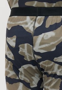 Kamo raštų legginsai bežo, rudos ir tamsiai mėlynos spalvų atspalviuose. Su juodu elastingu juosmeniu ir matomais siūlės įpjovimais.