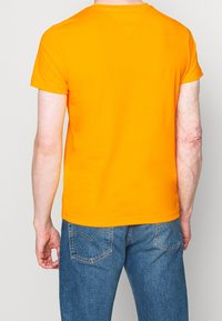 Camiseta de manga corta en naranja brillante, hecha de algodón suave, con un escote redondeado y un diseño ajustado y sencillo.