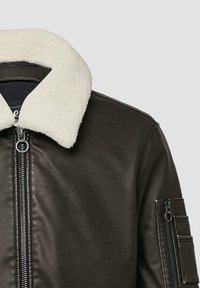 Braune Lederjacke mit einem cremefarbenen Kunstfellkragen, Front-Reißverschluss und einer Seitentasche mit Reißverschlussdetail. Glatte Textur und Ausführung.