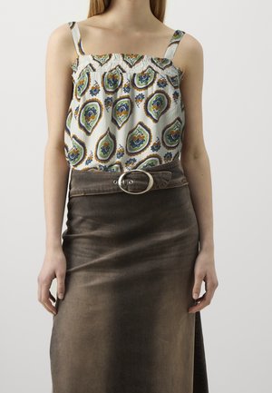 Woman wearing a white sleeveless top with green and orange floral patterns tucked into a dark brown skirt with a large silver buckle belt.