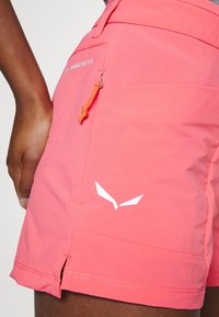 Shorts DuraStretch en color rosa con un bolsillo lateral, cordón naranja y detalle del logo en blanco. Presentan una textura suave y aberturas en ángulo en el dobladillo.