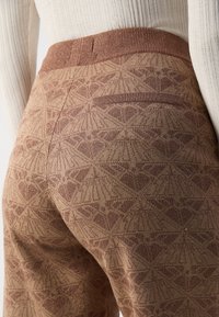 Pantalons marron à motifs avec un tricot texturé, présentant une taille côtelée contrastante et une petite poche arrière.