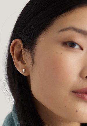 Hopeakorvakoru korvassa, soikea muoto ja sileä pinta. Lähikuva näyttää ihon sävyt ja hiusten yksityiskohdat, häiriötekijöitä on vähän.