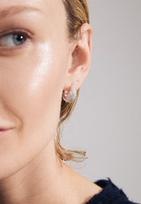 Guldtonade hoopörhängen med en böjd form som är prydda med små, klara kristaller för en glittrande textur och detalj.