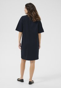 Navy blue short-sleeve dress in a loose fit, with a straight hem and soft texture. Paired with black flat shoes.
