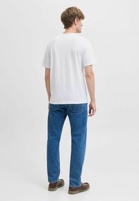 Weißes Baumwoll-T-Shirt mit kurzen Ärmeln, kombiniert mit blauen Jeans und braunen Schuhen. Die Rückansicht zeigt ein schlichtes Design und einen regulären Schnitt.