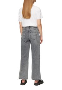 Graue, weite Jeans mit hoher Taille, fünf Taschen, sichtbaren Nähten und einem verblassten Finish, kombiniert mit einem weißen T-Shirt und schwarzen Schuhen.