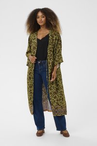 Garšs zaļš kimono ar paisley rakstu, atvērts priekšpuses, puskājas; vilkts virs melna topa un zila džinsu biksēm, ar dekoratīvu apdari pie apakšmalas.