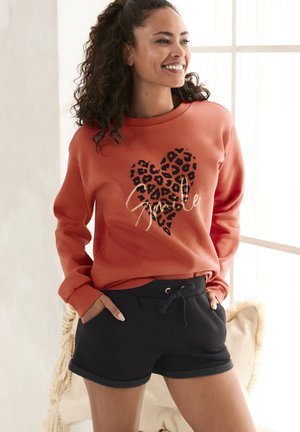 Rust-colored sweatshirt with black leopard heart design and "Smile" text, paired with black shorts featuring a drawstring waist and rolled hem.