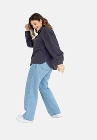 Ciemnoszara koszula zapinana na guziki z kieszonką, połączona z jasnoniebieskimi spodniami o szerokich nogawkach i białymi trampkami, prezentująca swobodny krój i casualowy styl.