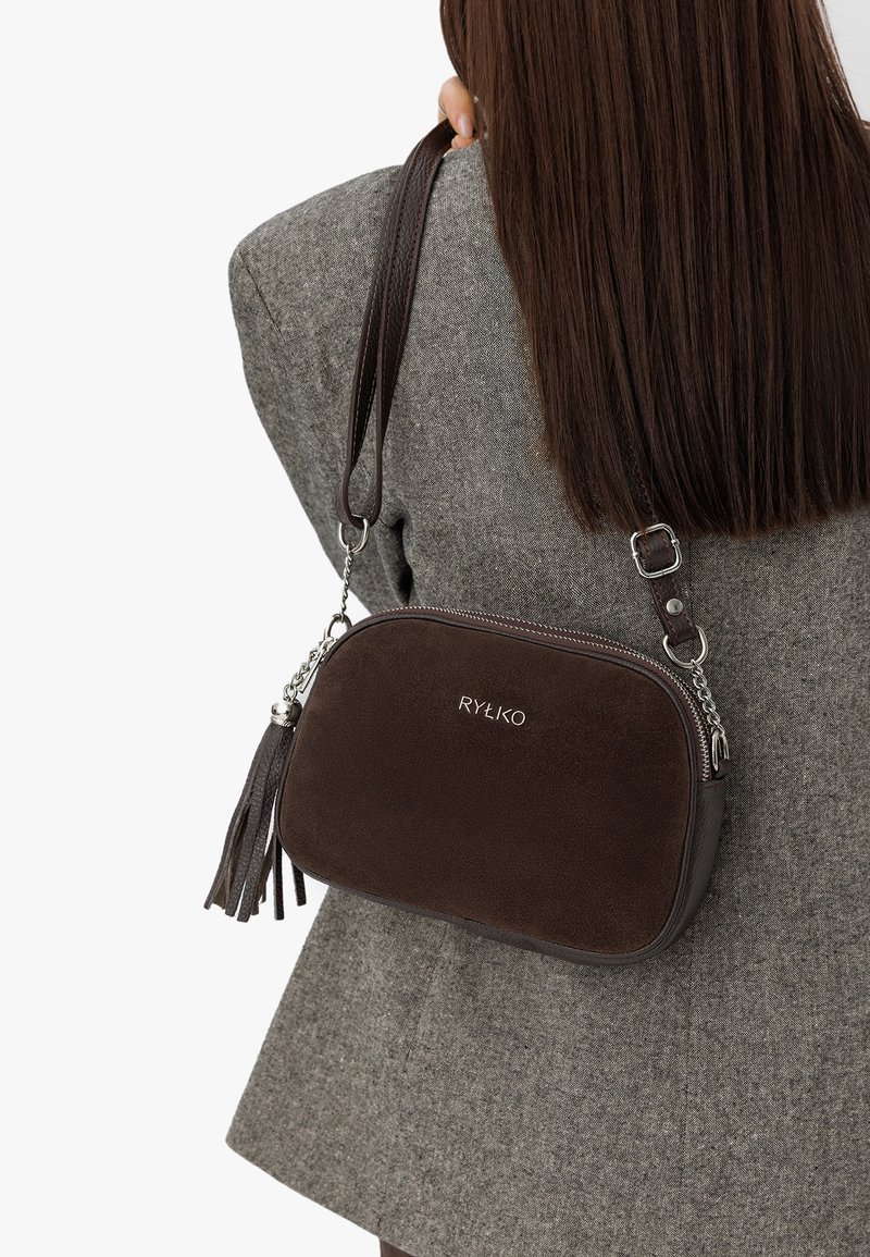 Borsa a tracolla in suede marrone con accenti in catena argentata, dotata di chiusura con zip e dettaglio con frangia. Logo impresso sul davanti.