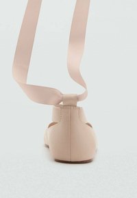 Ballerines en matériau rose clair avec un bout rond et une bride à l'arrière dotée d'un long ruban à nouer. Texture lisse, design minimaliste.