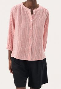 Camisa de botones a rayas rojas y blancas con cuello redondo y mangas de tres cuartos, combinada con pantalones cortos negros. Tejido ligero y texturizado.