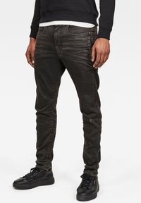 Tmavě šedé džíny se Slim fit, s vybledlým vzhledem, pěti kapsami a knoflíkovými detaily poblíž bočních švů, v kombinaci s černými teniskami.