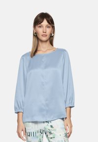 Light blue satin blouse with 3/4 length sleeves, round neckline, and subtle sheen. Paired with patterned, multicolored pants.