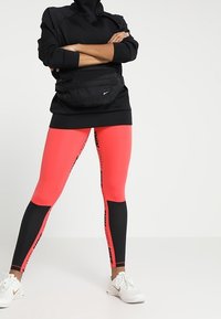 Černá mikina s kapucí, růžovo-černé legíny s potiskem loga a bílé tenisky. Černá ledvinka nošená v pase. Hladká tkanina, přiléhavý střih.