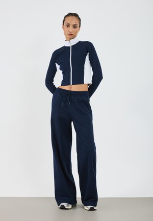 Tenue de sport bleu marine composée d'un sweat à zip court avec des panneaux latéraux blancs et d'un pantalon ample avec une taille élastique.