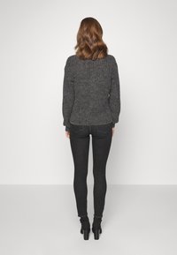 Suéter de punto gris oscuro con un acabado texturizado, forma ajustada y puños acanalados, combinado con jeans negros ajustados ybotines.