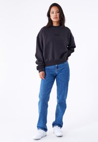 Dark gray oversized sweatshirt with ribbed cuffs, paired with light blue denim jeans. Model stands against a plain white background.