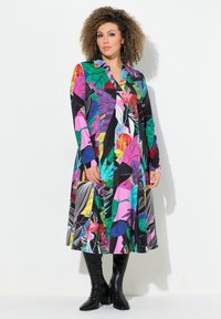 Langes Hemdkleid mit einem lebhaften Blumen- und Blätterdruck in Pink, Grün, Blau und Schwarz. Besitzt einen kragenförmigen Ausschnitt und eine durchgehende Knopfleiste.