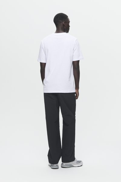 Baltas īsām piedurknēm T-krekls saskaņots ar brīviem melniem biksēm. Pelēki sporta apavi noslēdz apģērbu. Vienkāršs dizains, minimāls apdare.