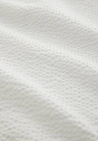 Tissu blanc texturé avec un motif subtil de points en relief, présentant une surface douce et lisse ainsi qu'un léger drapé.