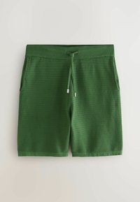 Shorts en maille texturée verte avec taille élastique, cordon de serrage à l'avant et poches latérales, posés à plat sur une surface claire.