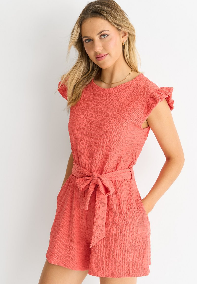 Coral romper with short ruffled sleeves, textured fabric, belted waist, and side pockets; casual, comfortable design.