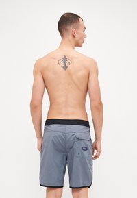 Pantaloni da nuoto grigi con elastico nero in vita, dotati di tasca posteriore e patch con logo, realizzati in tessuto leggero. Nessun motivo visibile.