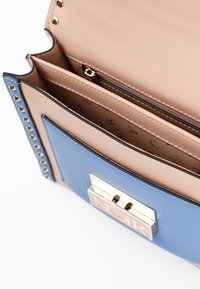 Borsa blu e beige con texture trapuntata, dotata di un clasp centrale con finiture in oro e borchie lungo i lati. Interno con tasca con zip.