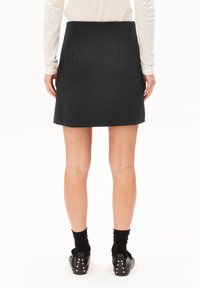 Femme portant une mini-jupe noire, des chaussettes noires et des chaussures noires avec des clous argentés, debout, dos à la caméra.