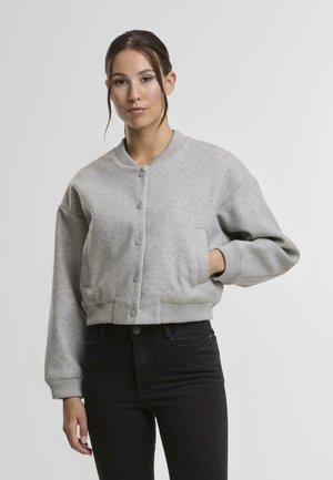 Pulover scurt gri, cu nasturi în față, guler rotund și manșete cu nervuri. Confecționat dintr-un material moale, are buzunare laterale. Este asortat cu blugi negri.