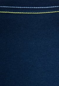 Dunkelblaues Baumwollgewebe mit gerippter Textur und einer auffälligen gelb-blauen Naht an der Oberseite. Glatte Oberfläche mit leichtem Glanz.