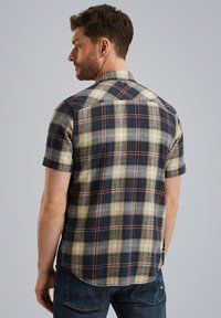 Chemise à manches courtes à carreaux dans des nuances de bleu marine, beige et rouille. Le tissu présente un tissage texturé, avec un ourlet arrondi et des détails sur le dos.