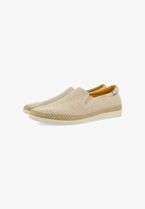 Zapatos de slip-on beige con parte superior de malla, forro interior amarillo y suela de yute trenzado. Presentan una punta redondeada y suela de goma.