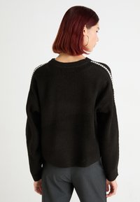 Maglione nero lavorato a maglia con una vestibilità comoda, caratterizzato da una texture rigata e cuciture bianche lungo le cuciture delle spalle.