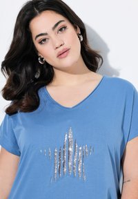 Camiseta corta de manga corta azul con escote en V, que presenta un diseño de estrella brillante en la parte delantera. Tejido suave con un corte relajado.