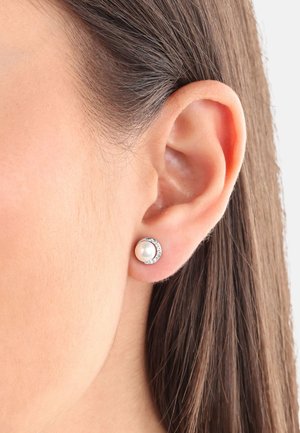 Orecchini a perno con perle e accenti in argento, caratterizzati da una perla bianca rotonda circondata da una montatura in argento texturizzato. Primo piano dell'orecchio.