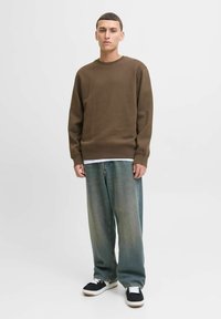 Bruin katoenen sweatshirt met een ronde hals, gecombineerd met losse, vervaagde denim jeans. Zwart-witte sneakers maken de look compleet.