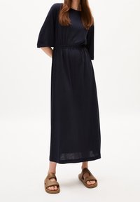 Laivastonsininen maksimekko, jossa on lyhyet hihat, nyörityksellä kiristetty vyötärö ja pehmeä kangas. Yhdistetty ruskeisiin liuku-sandaaleihin, joissa avoin varvas.