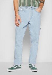 Jean en denim bleu clair avec une coupe droite, dotés de poches avant, d'un patch de la marque sur la poche arrière, complétés par des baskets en daim vert.