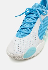 Zapatilla deportiva azul con parte superior de malla, material perforado blanco y acentos en azul claro. La suela de goma blanca presenta un patrón de espiga.