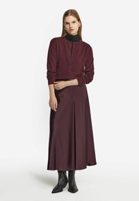 Burgundy stickad cardigan med långa ärmar och framknappar, matchad med en lång satin kjol och svarta spetsiga ankelboots.