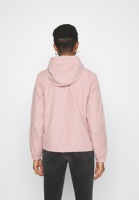 Ljusrosa hooded jacka med en mjuk textur, elastiska ärmslut och midjeband. Bakifrån syns sömnadsdetaljer och en avslappnad design.