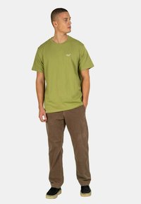 Olive green cotton t-shirt with a crew neck and short sleeves, paired with brown corduroy pants and black shoes with a beige sole.